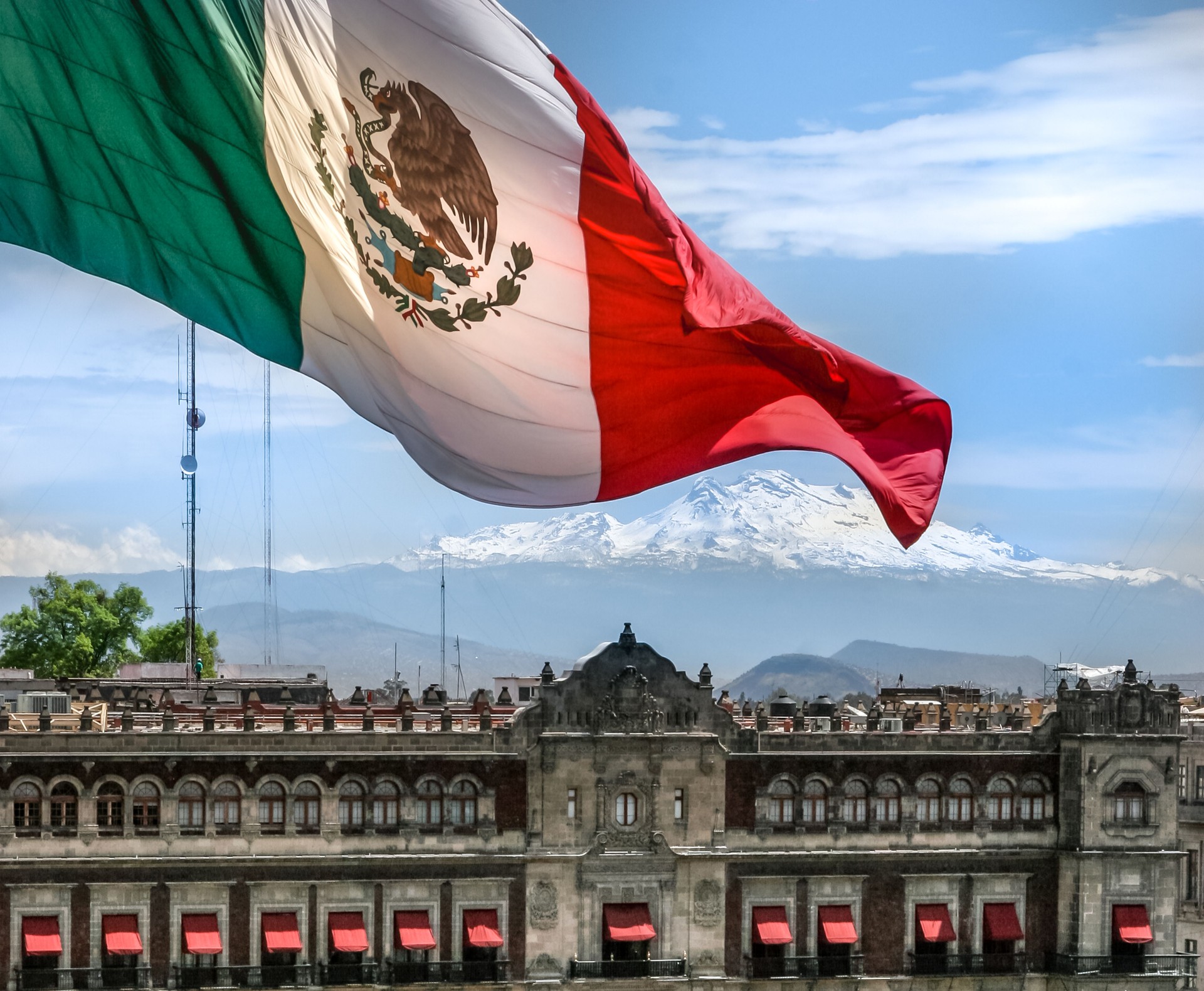 The monumental flag of Mexico flies in the heart of Mexico City with the Iztaccihuatl Volcano on the horizon The monumental flag of Mexico flies in the heart of Mexico City with the Iztaccihuatl Volcano on the horizon